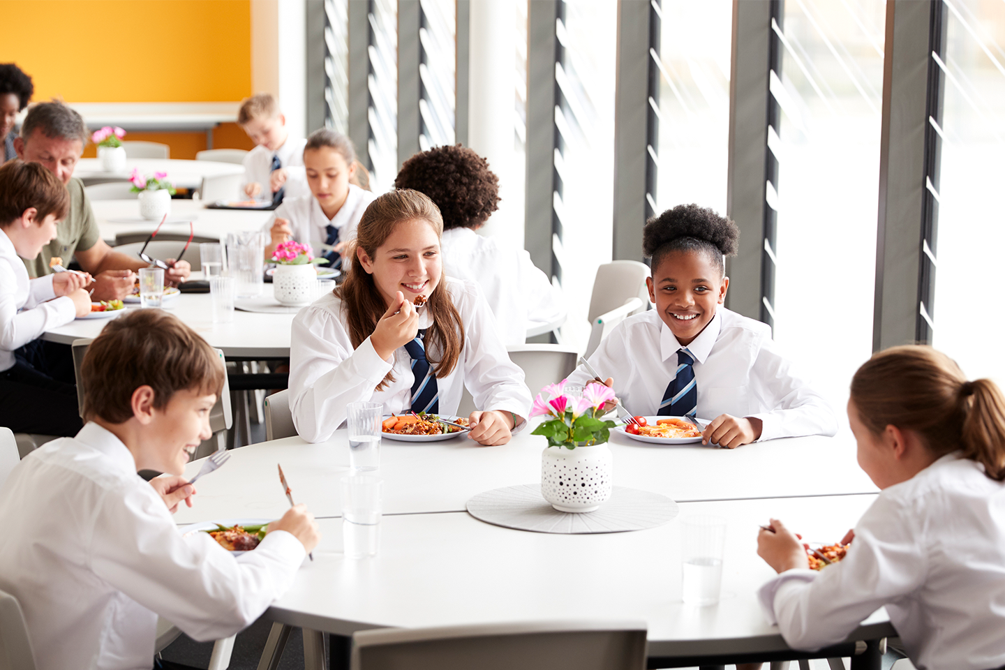 Photo of group of students in school uniform around tables eating breakfast