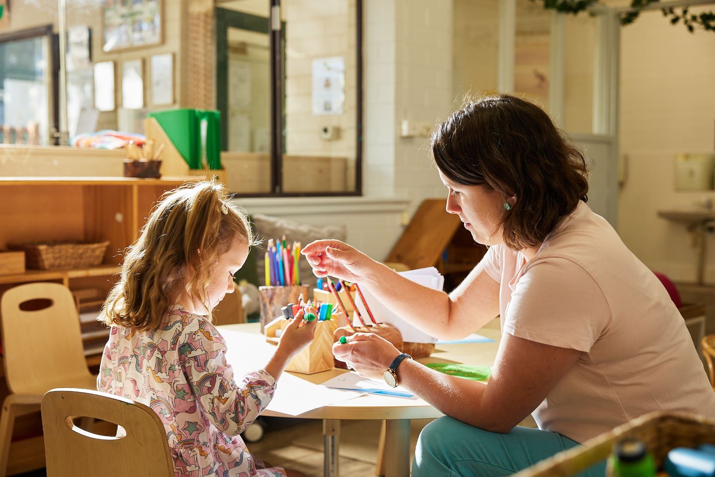 Female kindy educator sitting at a table with a child.