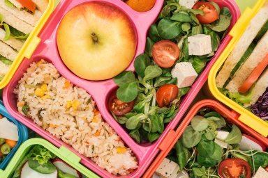 Zoomed in photo of colourful school lunchboxes with fruit, sandwiches and salads