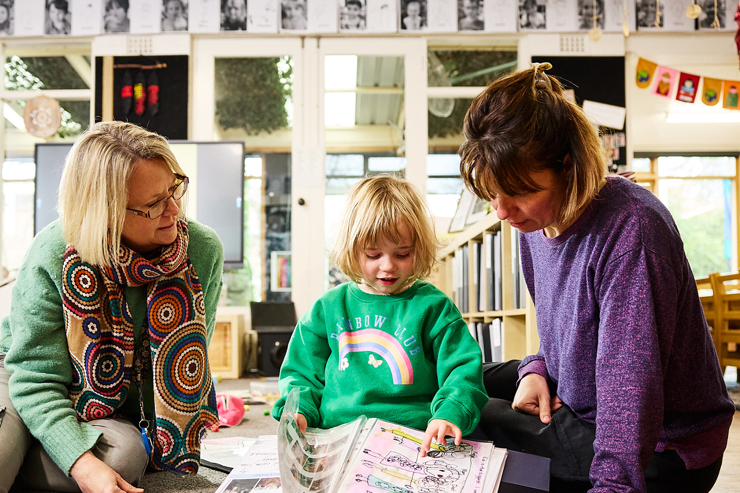 Photo of preschool student reading with two preschool teachers