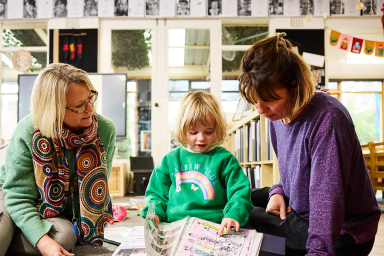 Photo of preschool student reading with two preschool teachers
