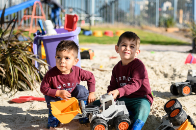 Photo of two preschool children playing with toy trucks in sandpit