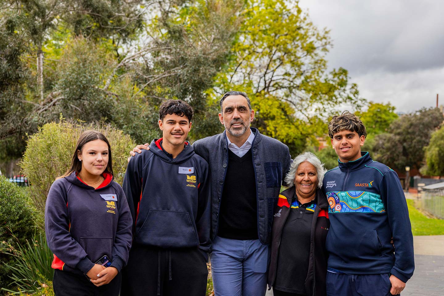 Students and staff standing alongside AFL great Adam Goodes