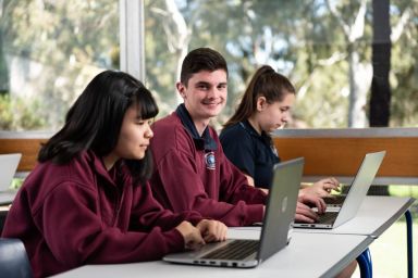 Three students working on laptop computers, sitting side by side