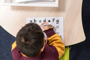 Birds-eye view (looking down from above) photo of a primary school student tracing the alphabet on a small whiteboard