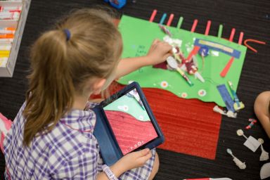 One student, holding an iPad, in a classroom 