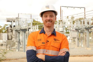 male in hi-vis top standing in front of an electricity site.