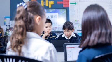 Four students, completing work in class, viewing the work on a computer