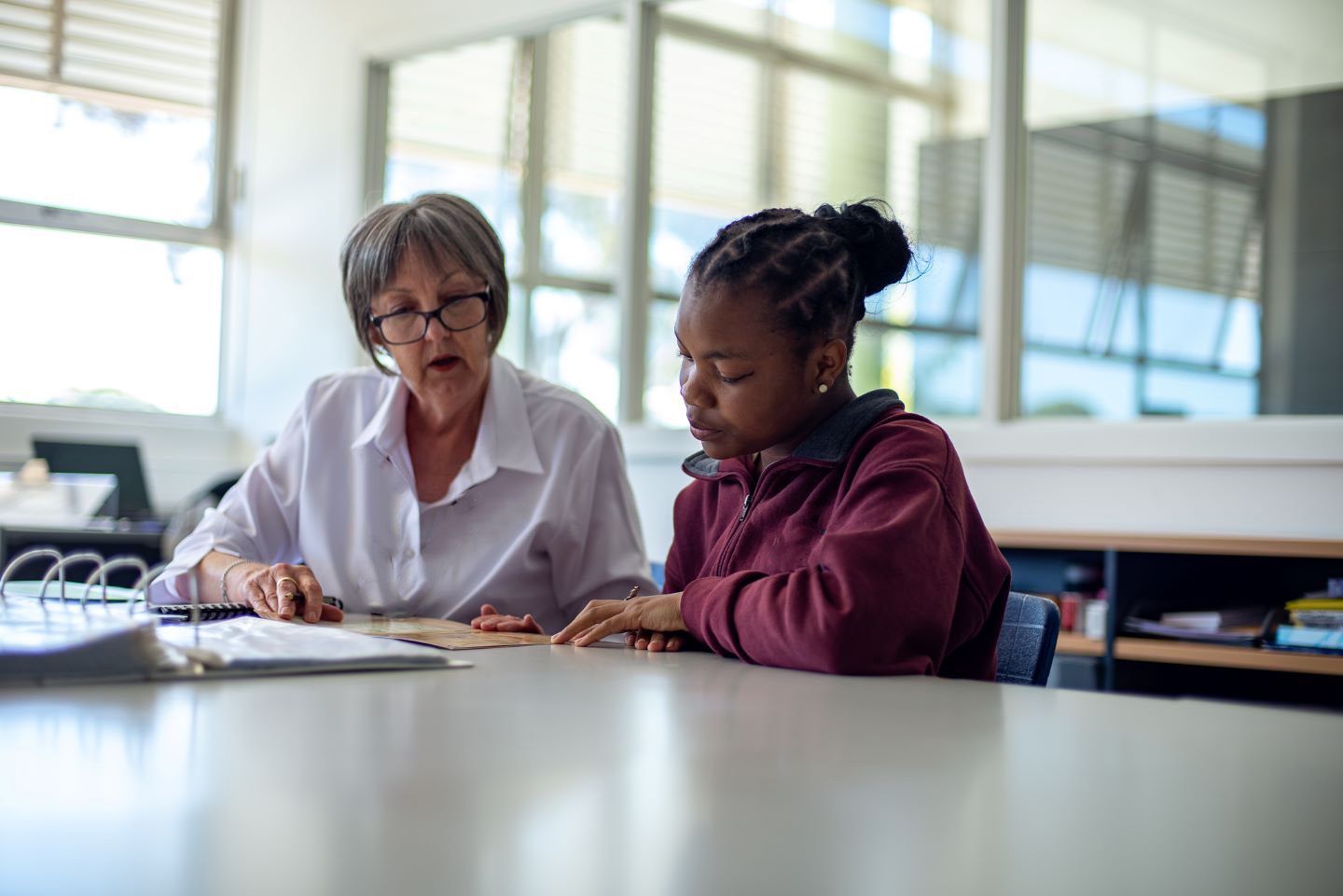 High school student sitting at a desk with her teacher.