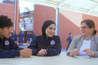 Three people, two of them are students one of them are a teacher, sitting together, conversing 