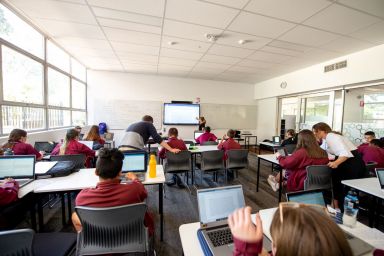 Classroom full of students, sitting down while teachers assist students