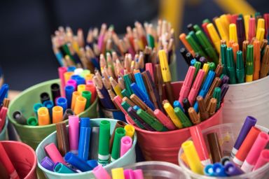 Close up photo of coloured pencils in cups, in a school classroom
