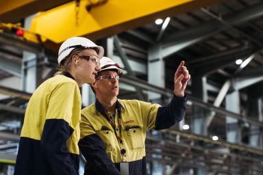 Two people wearing hard hats and high vis clothing working in an industrial workshop