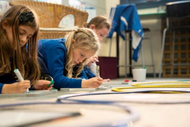 3 Students, Primary School students, sitting at a table, writing on a piece of paper 