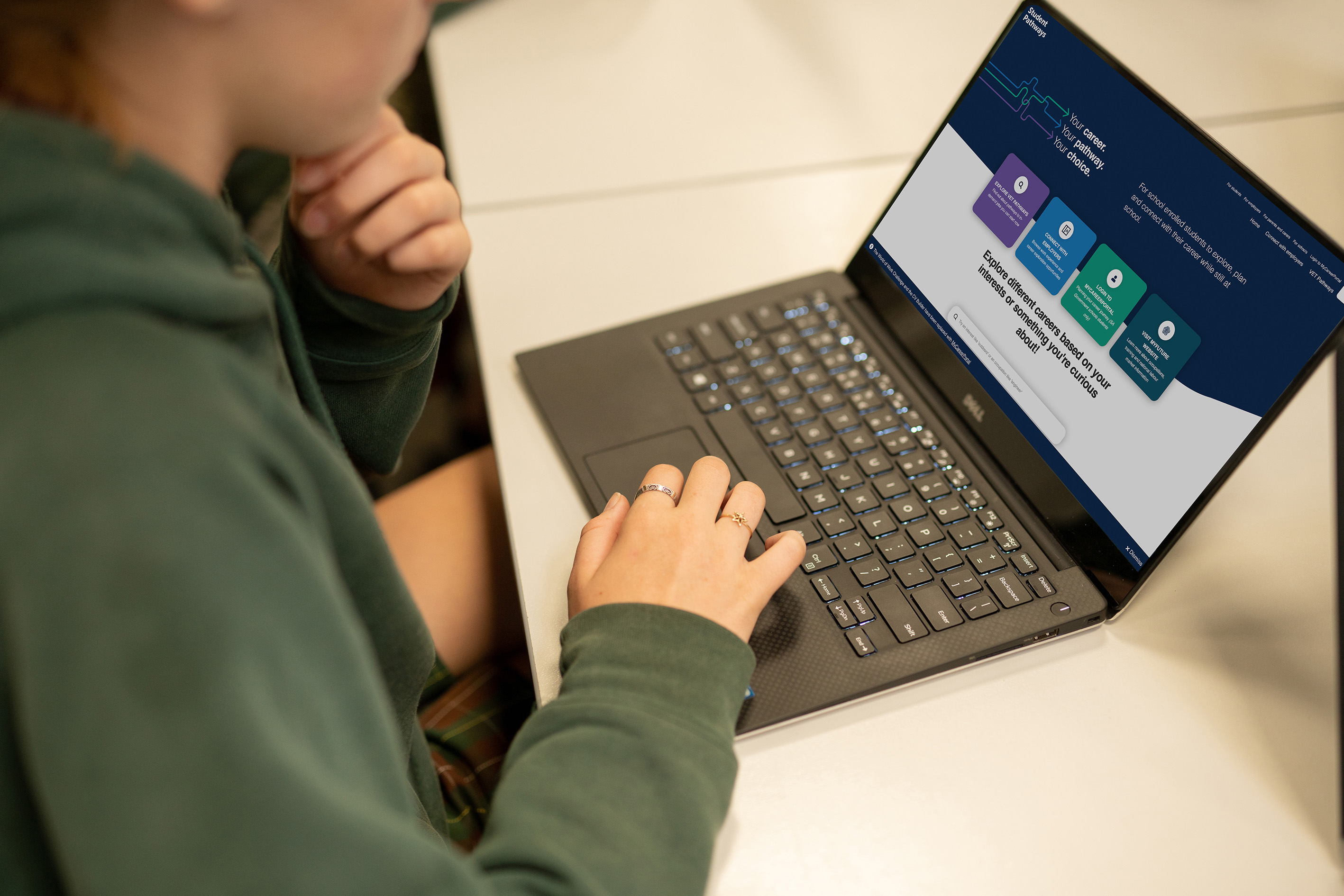 Student, using a laptop, at a table, close up shot, not able to see student 