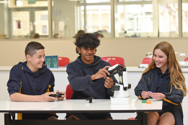 Photo of three students learning to use a robotic arm