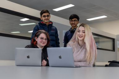 Four students looking at the screen of a laptop computer