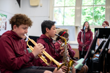 Photo of students playing brass musical instruments with students singing in background