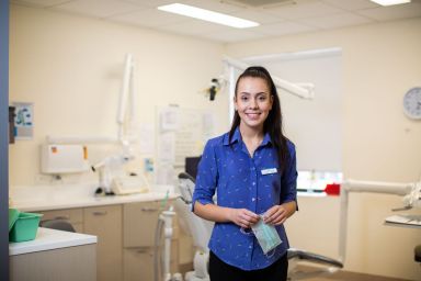 Young woman standing in a dental clinic holding a face mask. 