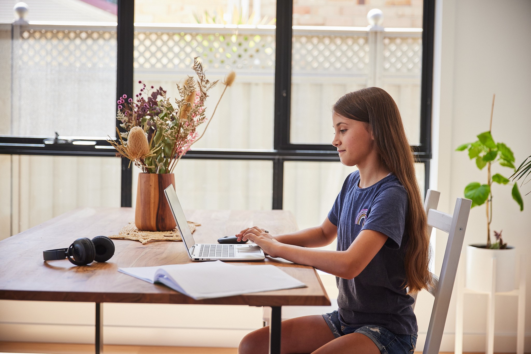 Young girl sitting at a dining table working on a laptop computer