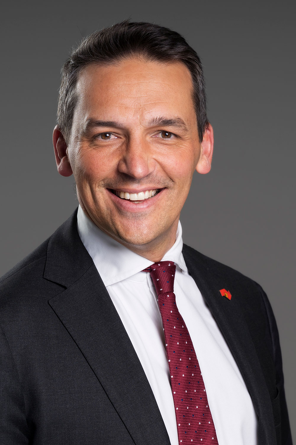 Blair Boyer, smiling and wearing a black suit with a white shirt and red tie.