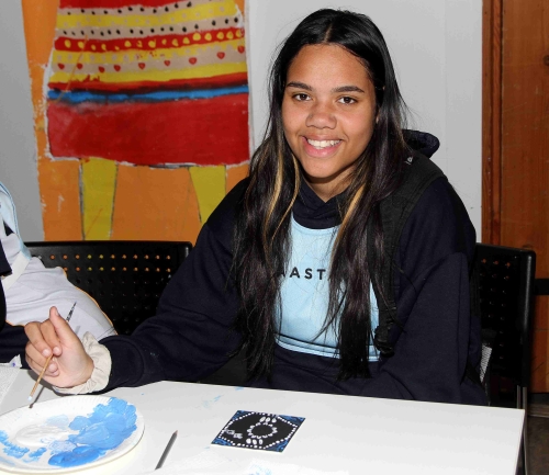 SAASTA student smiling and painting some art, with arworks behind them. 