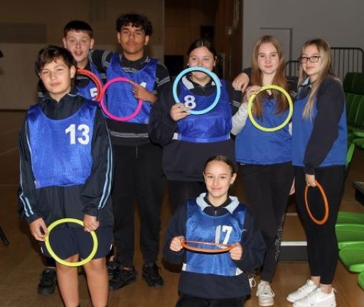 A team of 7 SAASTA students, holding colourful rings and wearing sports bibs. 