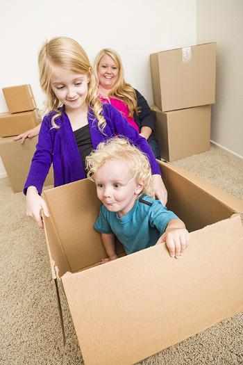 Boy and girl playing in a cardboard box while mother watches