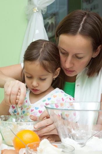 A mother shows her daughter how to bake a cake