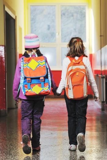 Two girl walking to class with their bags while holding hands