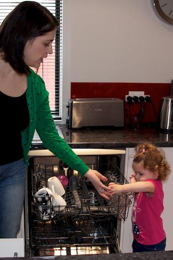A mother shows helps her daughter to unload the dishwasher.