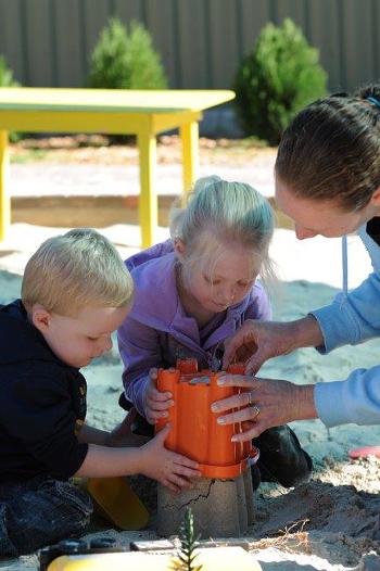 Young boy and girl making a sandcastle with an adult