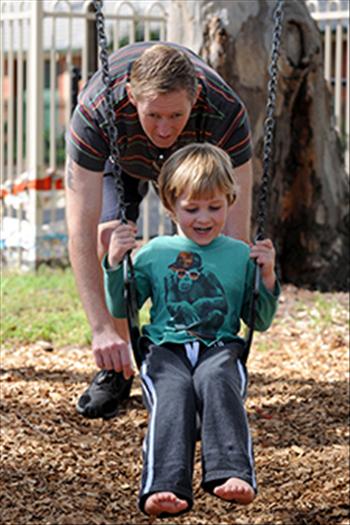 Father pushing young son on playground swing
