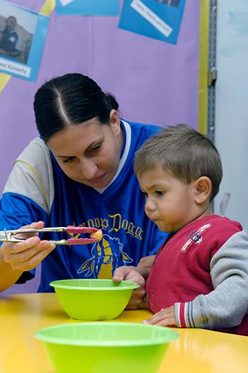 Adult showing toddler how to pick something up with tongs