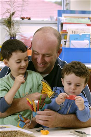 Two children playing with playdough while sitting on adults lap