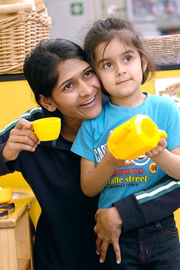 Adult and child playing with toy kettle and cup