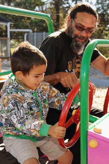 Young boy playing in a life size toy car with an adult male