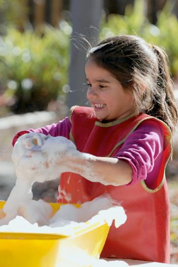 Young girl playing with soap suds in water