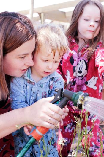 An adult and two children watering the garden together