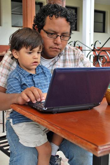 Young boy sitting on fathers lap looking at a laptop