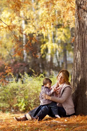 Mother and child sitting against a tree in Autumn 