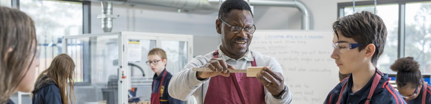 An educator using a ruler to measure a piece of timber while students look on.