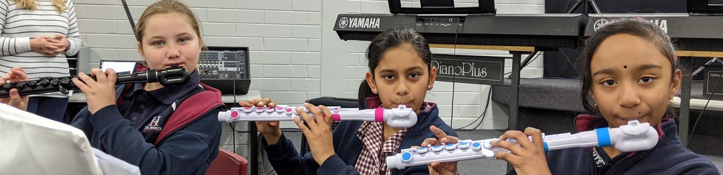 Three students playing the flute in a music room