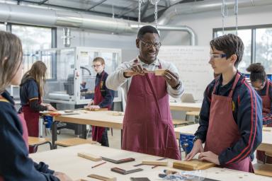 An educator using a ruler to measure a piece of timber while students look on.