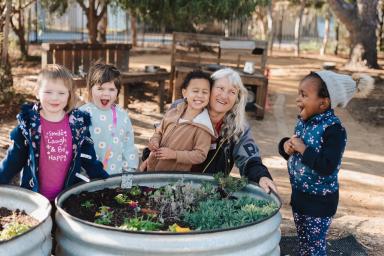 A preschool educator with 4 children, playing in the garden.