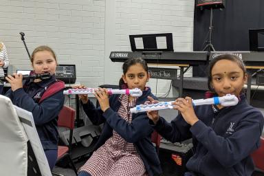 Three students playing the flute in a music room