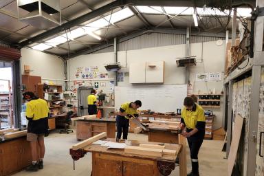 Students in high-vis clothing using tools in a workshop.