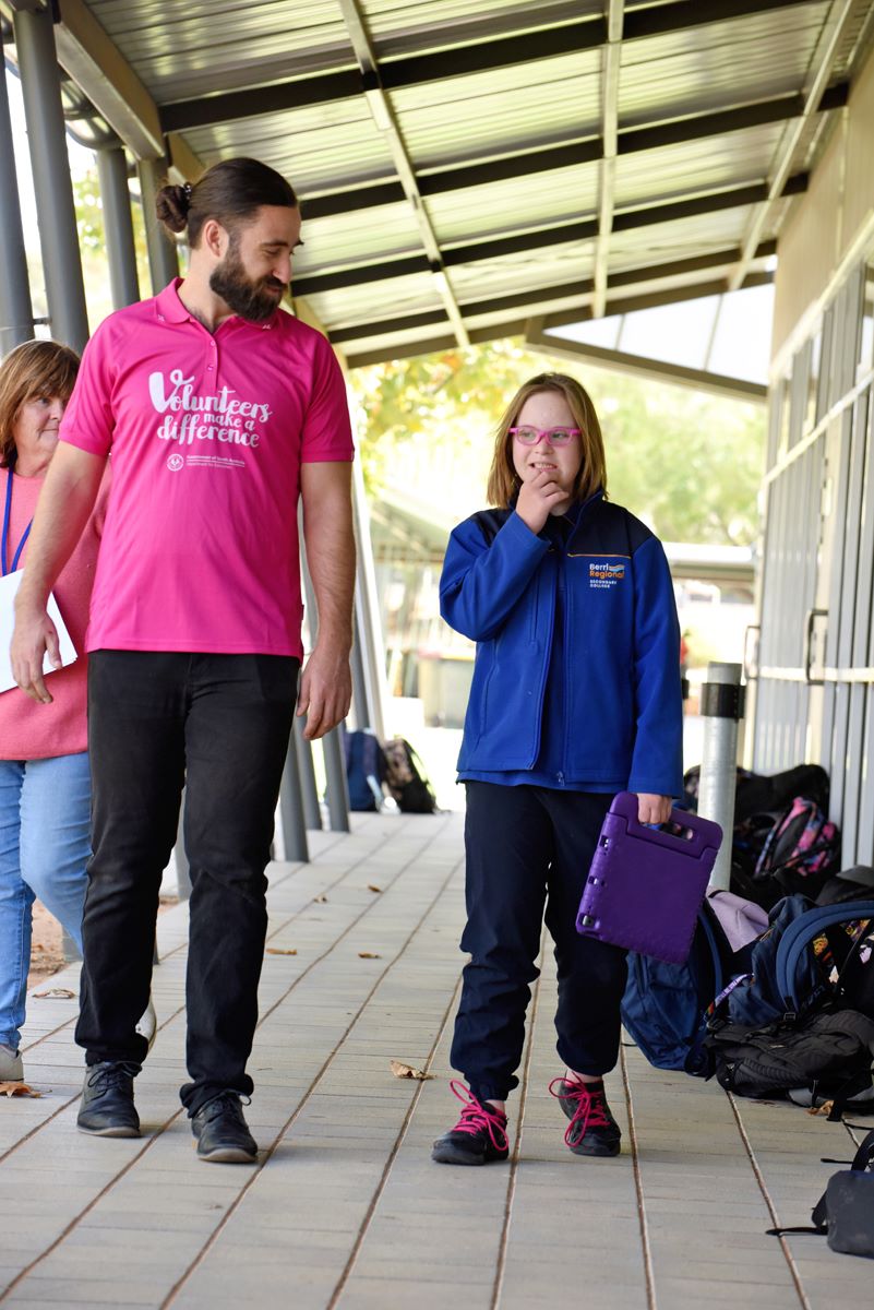 An adult volunteer walking outside with a student who is holding a tablet device.  