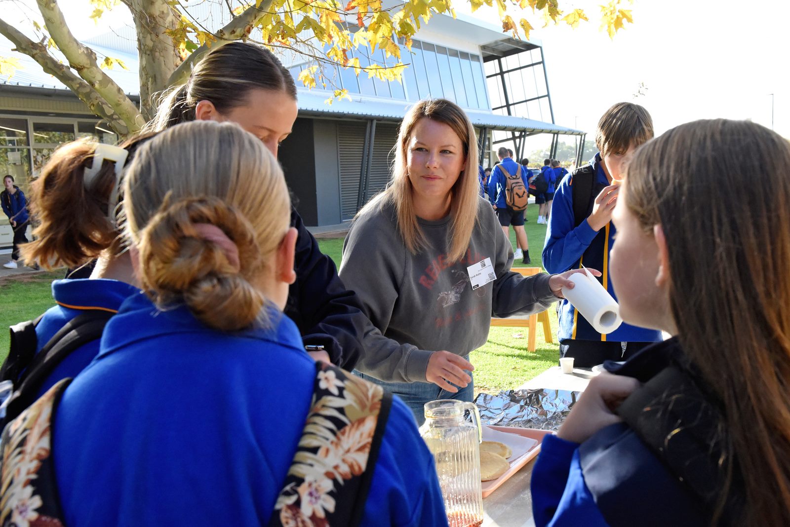 An adult volunteer at a school fair outside with some students, getting pancakes ready.