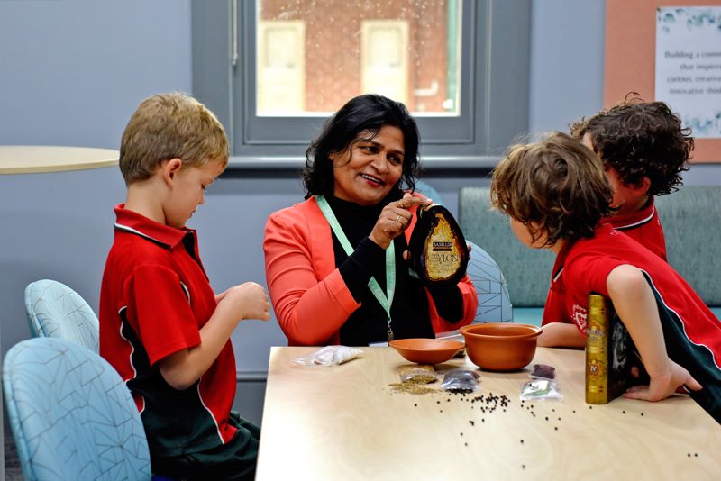 An adult volunteer with 3 students at a desk looking at some seeds.
